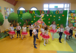 Dzieci tańczą ustawione w szeregu z rączkami na bioderkach, jedną nóżką tupią rytmicznie w podłogę.